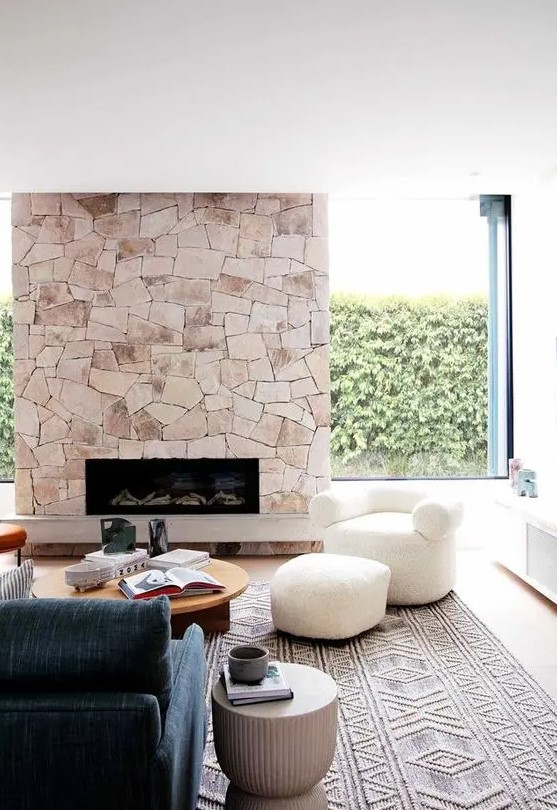 A modern living room with a stone fireplace, an indigo blue sofa, low coffee tables and a white chair and stool is wow