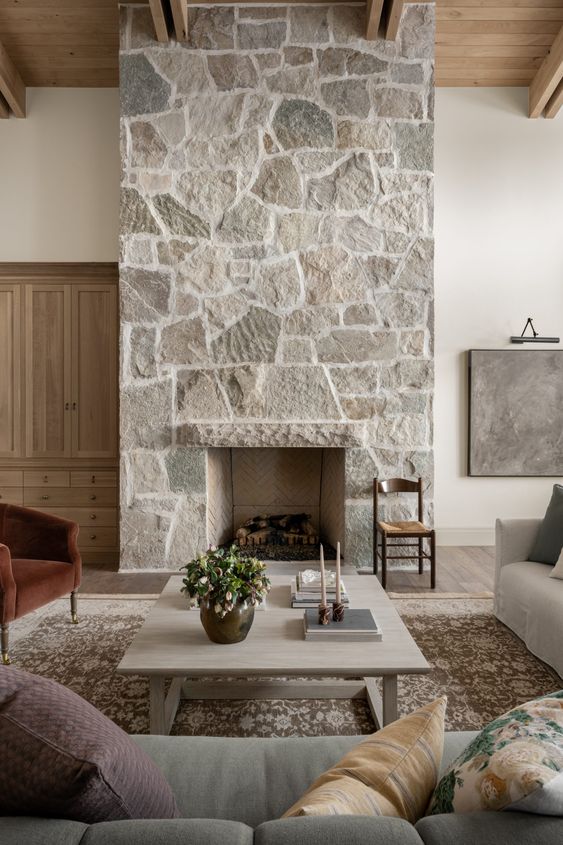 a modern living room with a stone fireplace, various seating in muted colors, a low coffee table and some decor