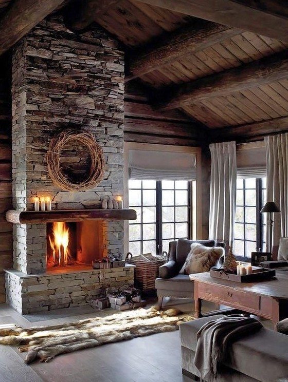 a moody, neutral living room with a gray stone fireplace, vintage furniture, faux fur rugs, blankets and candles