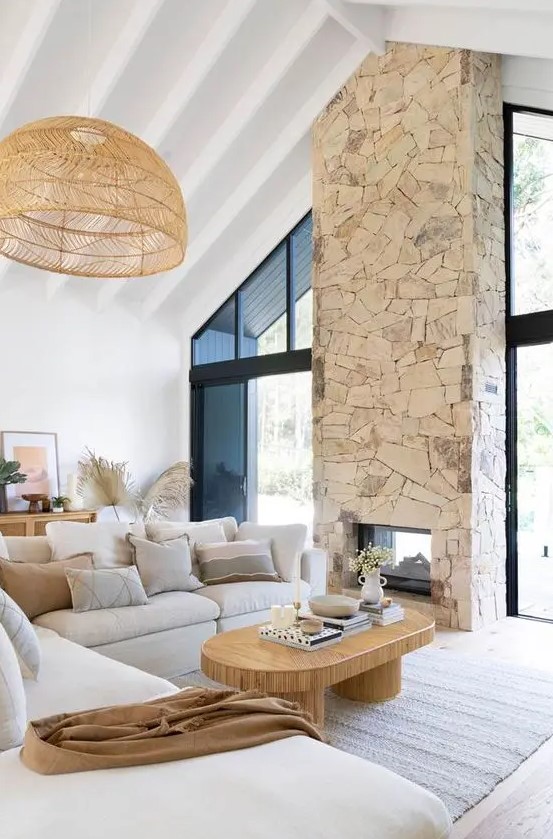 a neutral boho living room with a stone fireplace, a neutral side table, a low coffee table and a woven pendant lamp