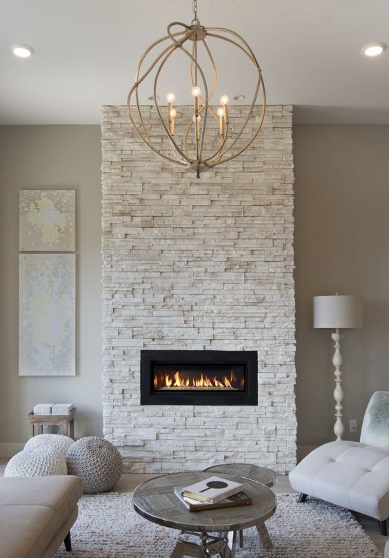 a neutral living room with a built-in faux stone-clad fireplace, neutral seating, coffee tables and a ball chandelier