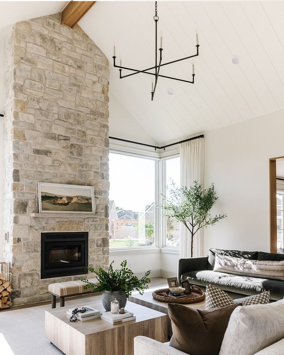 a neutral living room with a large stone-clad fireplace, a dark green and cream sofa, low coffee tables and lots of greenery