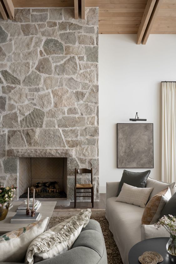 a neutral living room with a stone fireplace, neutral seating, a coffee table and some decor