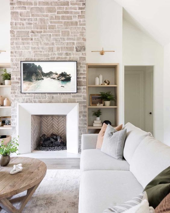 a neutral living room with a stone fireplace, a neutral sofa, muted-colored pillows, a stained coffee table, and some decor