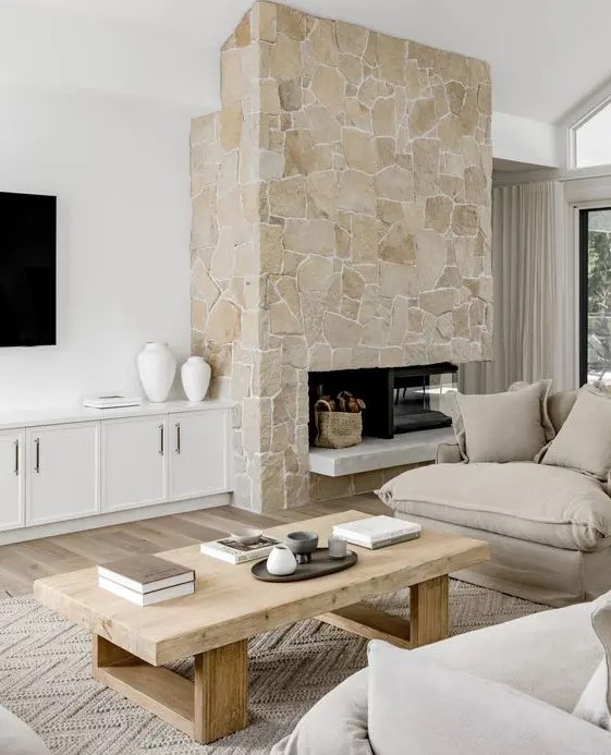 a neutral living room with a stone fireplace, neutral seating, a low coffee table and white built-in cabinets