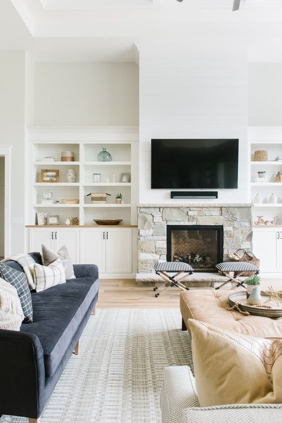 a neutral living room with built-in storage, a stone-clad fireplace, a television, a navy blue sofa and tan seating