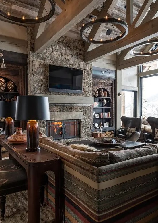 A stylish wood-clad chalet living room with a stone fireplace, boho and modern furniture and round chandeliers