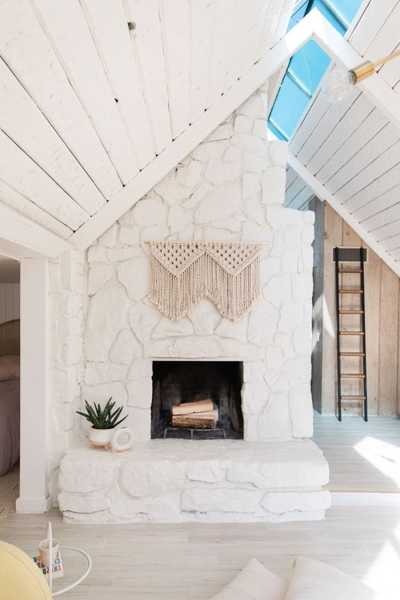 A white stone boho fireplace with macrame and potted plants is a cool and chic idea for a neutral space