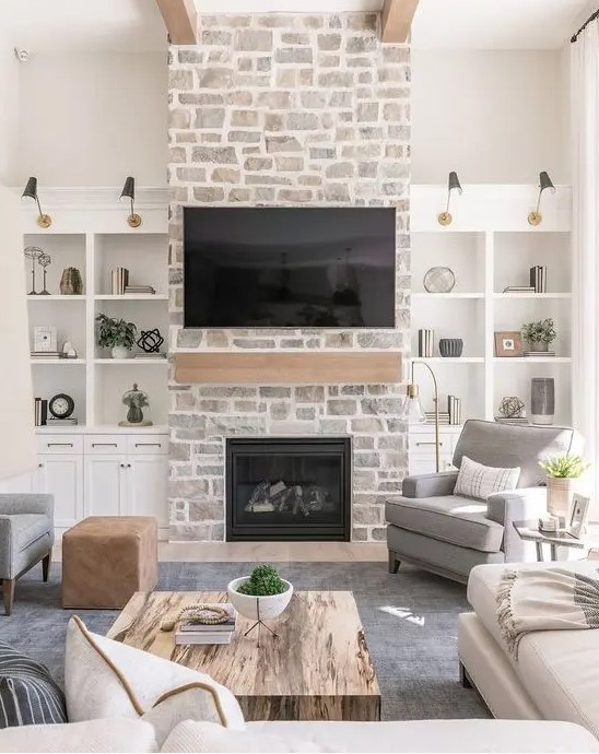 A whitewashed stone fireplace with a wooden mantel and storage compartments on either side adds a cozy and chic touch to the room's decor