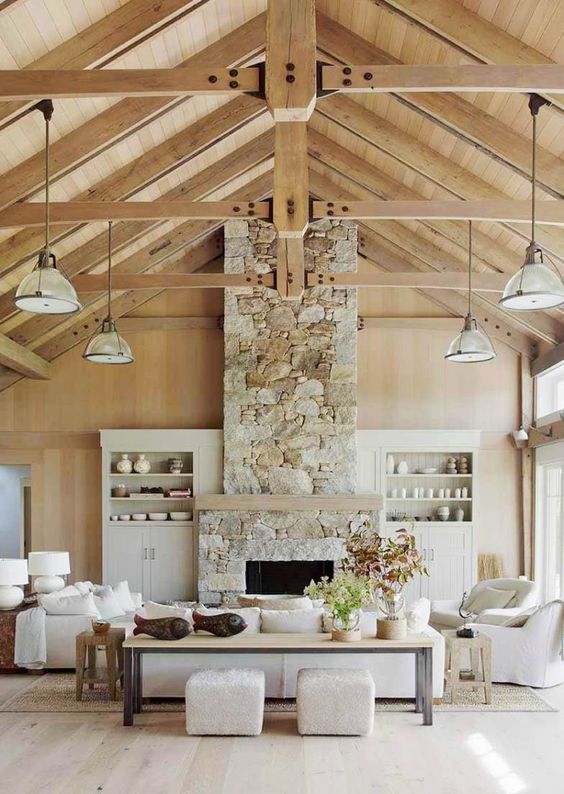 a living room in a coastal barn with a stone fireplace, neutral furniture and pendant lamps, and potted plants