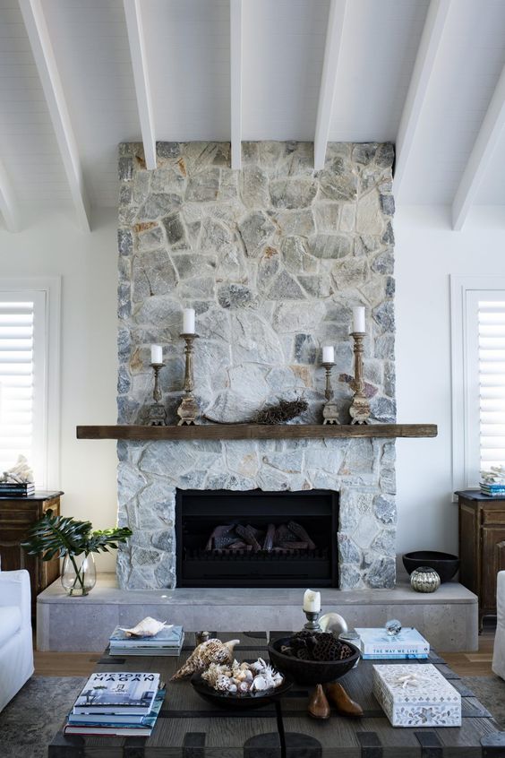 A modern coastal living room heated with a whitewashed stone fireplace, rough wood mantel and wooden candle holders