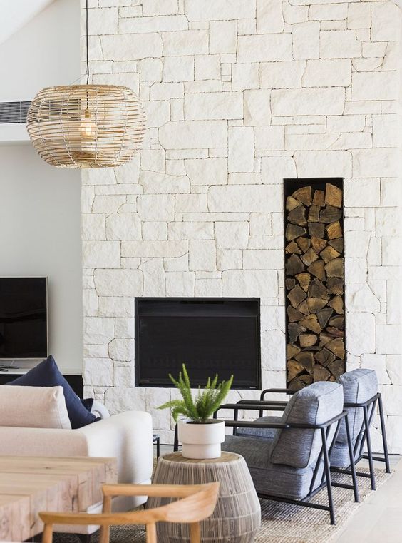 a modern coastal living room with an oversized white stone fireplace and a firewood alcove for a more inviting atmosphere