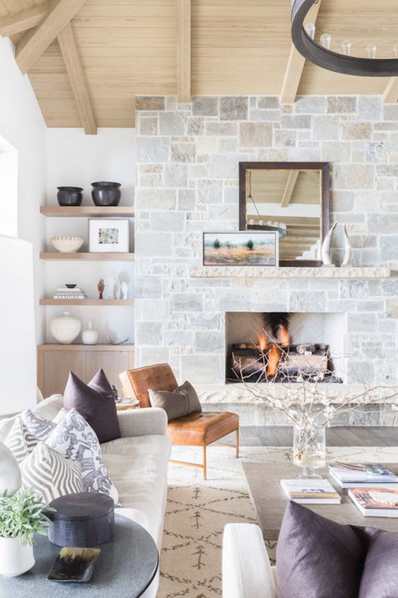 a neutral farmhouse living room with a stone fireplace, wooden mantel, artwork and a mirror that becomes the focal point here