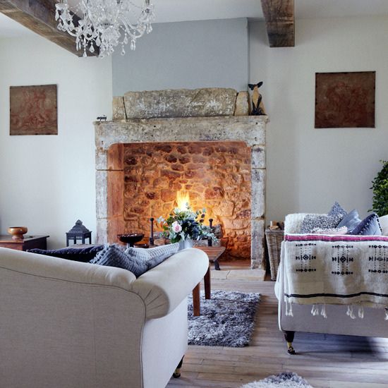 a neutral, sophisticated living room with a large vintage stone stove and some firewood and a lantern inside for more coziness
