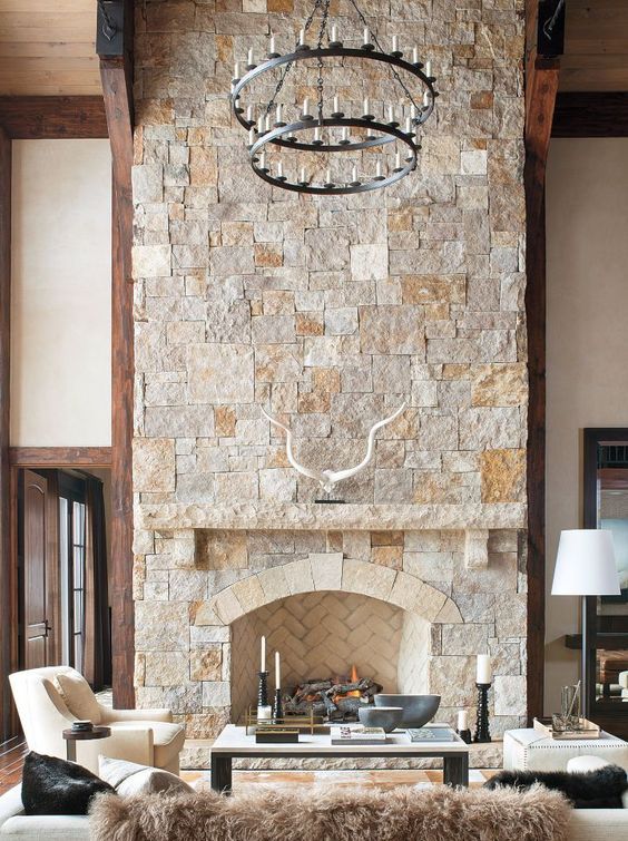 a neutral farmhouse living room with a stone fireplace, elegant cream furniture and a statement chandelier