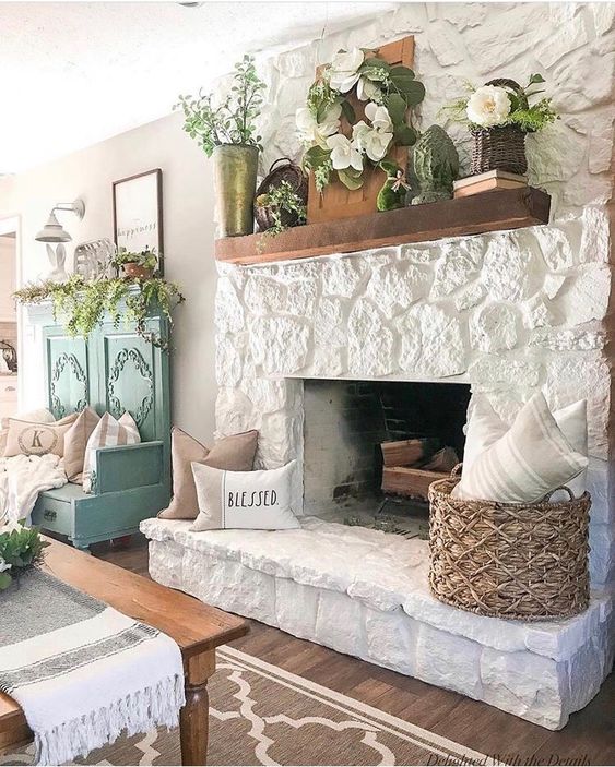 A vintage farmhouse style living room with a white stone fireplace, stained mantel, flowers and baskets is very inviting