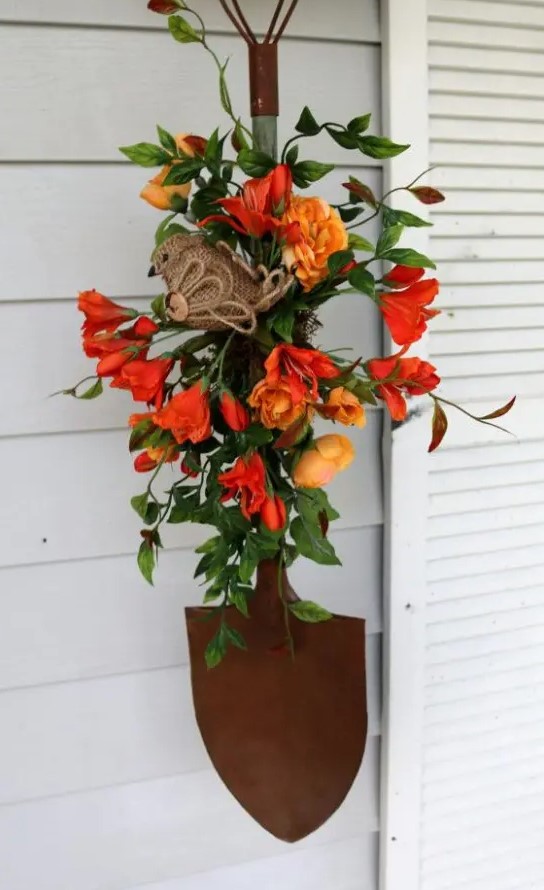 A bright artificial floral display with greenery, a burlap bird and a shovel makes a beautiful rustic outdoor decoration