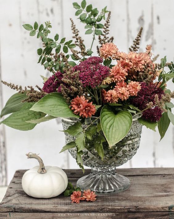 A chic and eye-catching fall floral arrangement in burnt orange and burgundy with leaves makes a cool and colorful decoration