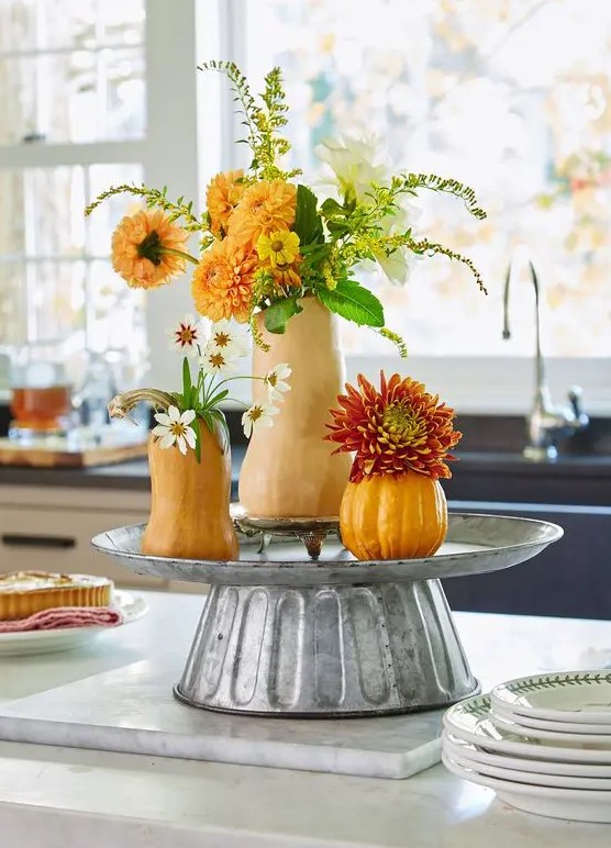 a cool rustic decoration made from a metal stand with pumpkins and gourds as well as greenery and artificial bright flowers