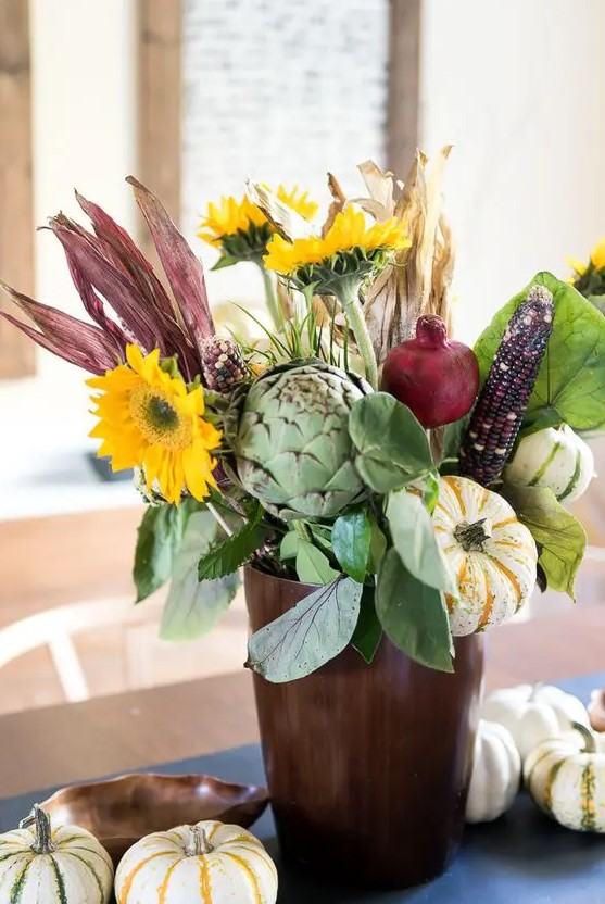 A farmhouse centerpiece made with artificial flowers, legumes, vegetables and some foliage is a cool fall decor idea