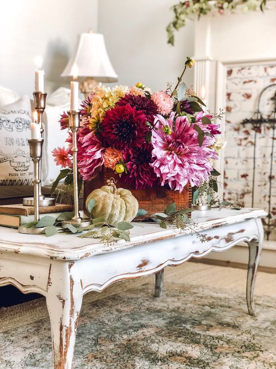 a beautiful and bold fall floral arrangement in burgundy, pink and yellow surrounded by natural greenery and pumpkins