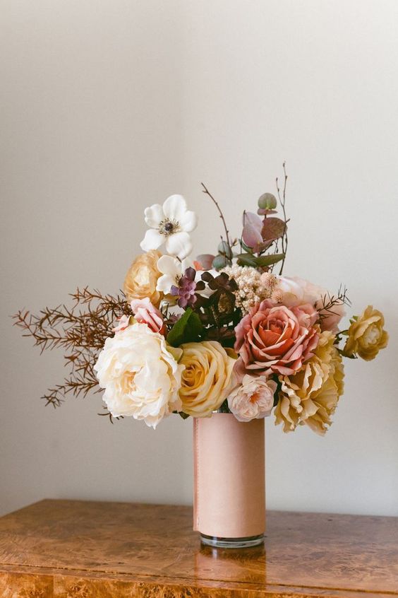 A pretty artificial flower arrangement in white, pink and yellow with dark leaves and branches that works in both summer and autumn