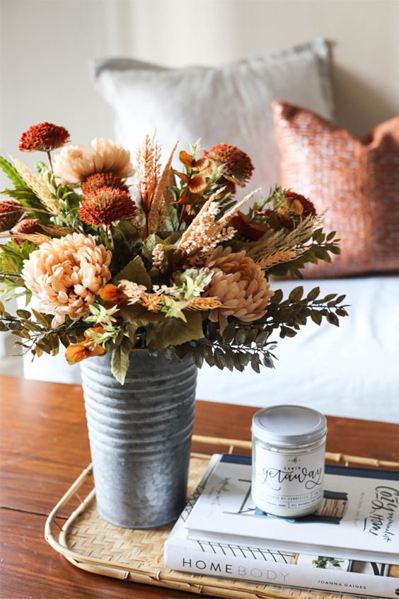 A beautiful, textured fall floral arrangement in burgundy, rust and blush with grasses and leaves placed in a metal bucket