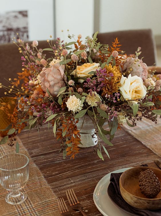 an atmospheric artificial flower arrangement in neutral tones, yellow, purple, mustard, with lots of green and strong leaves for autumn