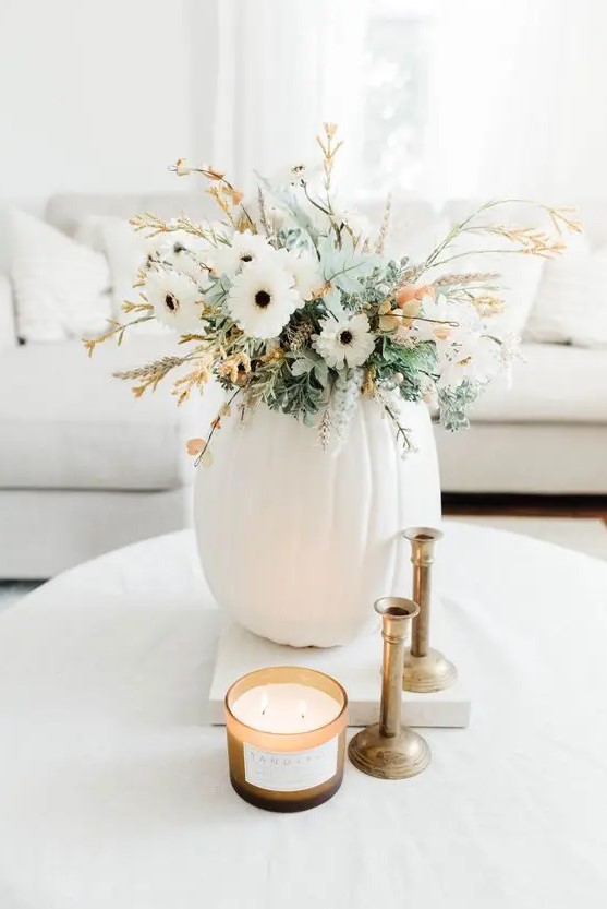 A neutral Thanksgiving centerpiece with a white pumpkin, white flowers, greenery and some flowering branches is cool
