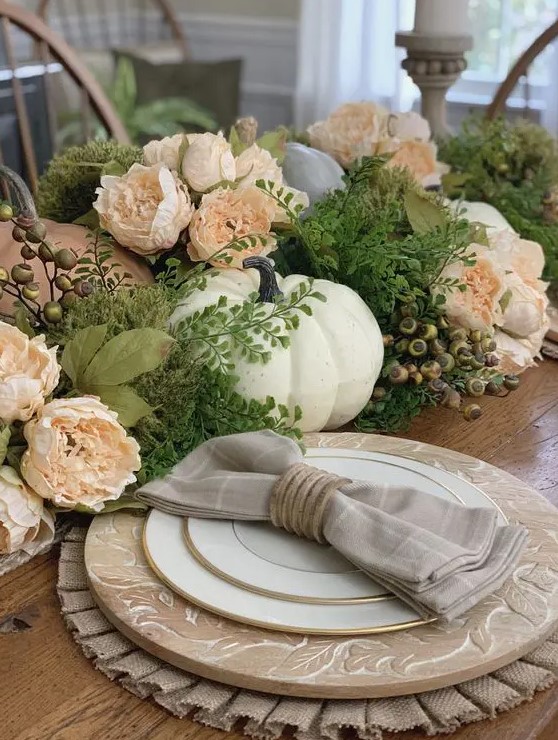 A pretty Thanksgiving centerpiece of greenery, berries, blush flowers, and white and light blue pumpkins is a chic solution