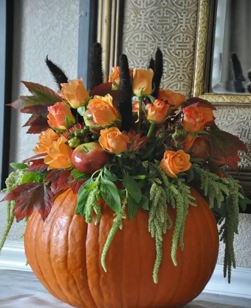 A pumpkin with greenery, artificial apples, artificial orange flowers and feathers makes a stylish centerpiece or decoration for fall
