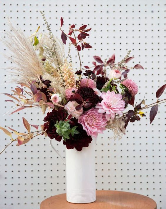A sophisticated faux floral arrangement in burgundy and pink, grasses and dark foliage makes an amazing focal point