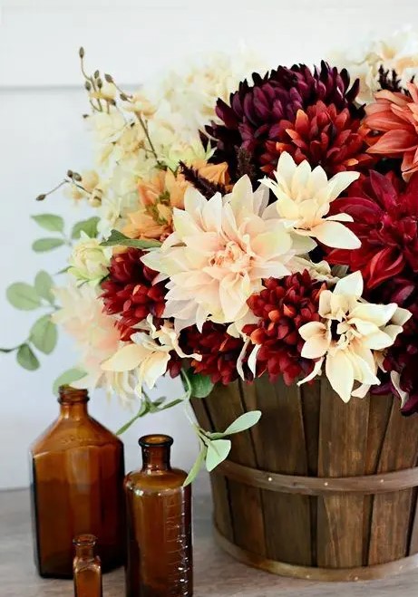 A stylish fall arrangement of blush, white and burgundy faux blooms in a basket is a cool, rustic piece to rock