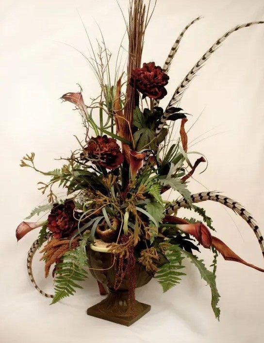 A stylish fall fall piece made from a vintage urn, greenery, feathers and artificial flowers is an elegant boho-inspired decoration for fall