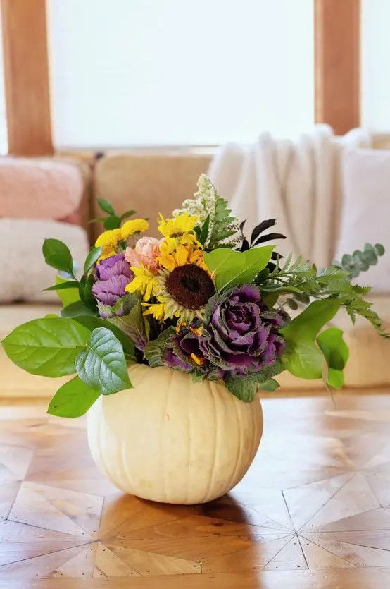 A white pumpkin with leaves, faux yellow and purple flowers, and some dried accents makes a chic fall centerpiece