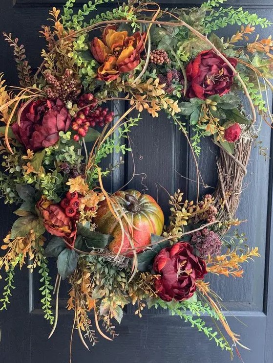 An autumn wreath made of leaves, artificial bright flowers, pumpkins and branches of various kinds is very chic