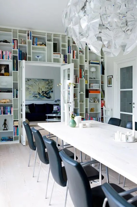 A dining room with a door wall occupied by open shelves displaying books, art, and candle holders is a cool idea for saving space