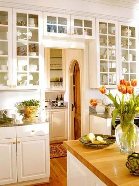 a white, modern farmhouse kitchen with shaker cabinets and glass cabinets, including those mounted over the door to create even more space