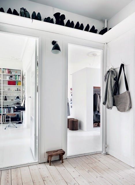 A white Scandinavian entryway with an open shelf above the doors for storing shoes and boots that are not being worn