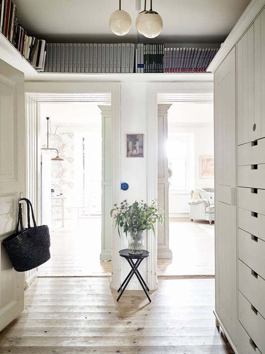 A white Scandinavian entryway with long shelves above the doors is great for storing a few things and displaying anything you want