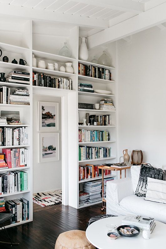 A white Scandinavian living room with an entire door wall taken up by bookshelves and display shelves to save a lot of space