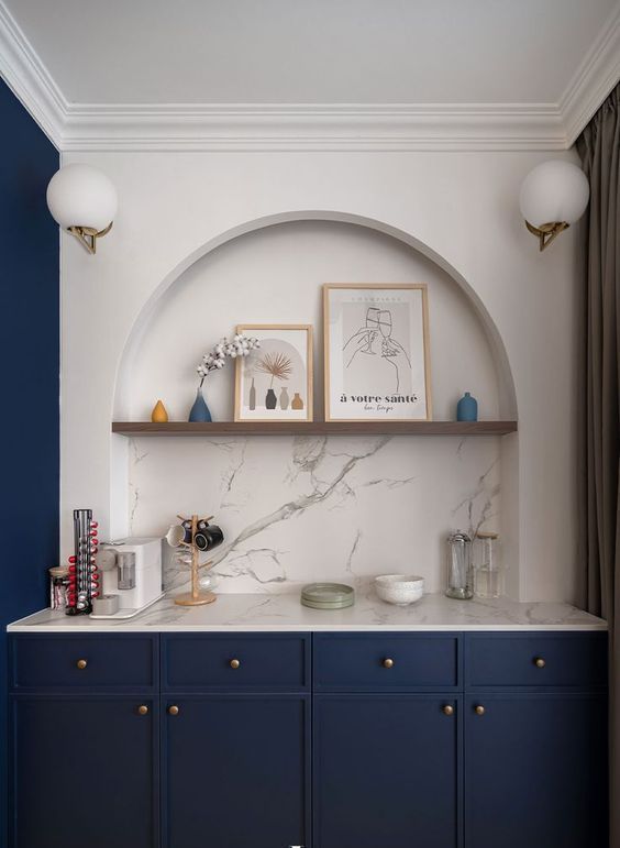 a refined space with an arched niche, navy cabinets, an open shelf, some decor and a coffee bar is a smart and elegant idea