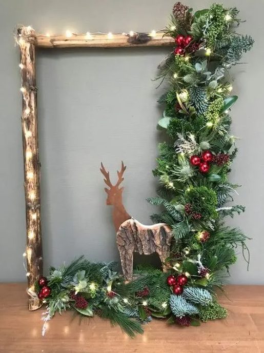 a rustic Christmas wreath with lights, evergreens, leaves, a wooden deer, berries and pine cones