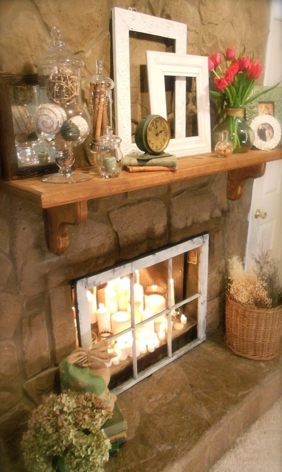 A candle arrangement of various candles in the fireplace and a vintage window covering it