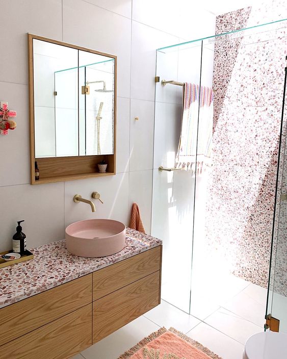 a catchy modern bathroom with a shower and a skylight, a stained vanity, pink terrazzo, a pink sink and a mirror cabinet