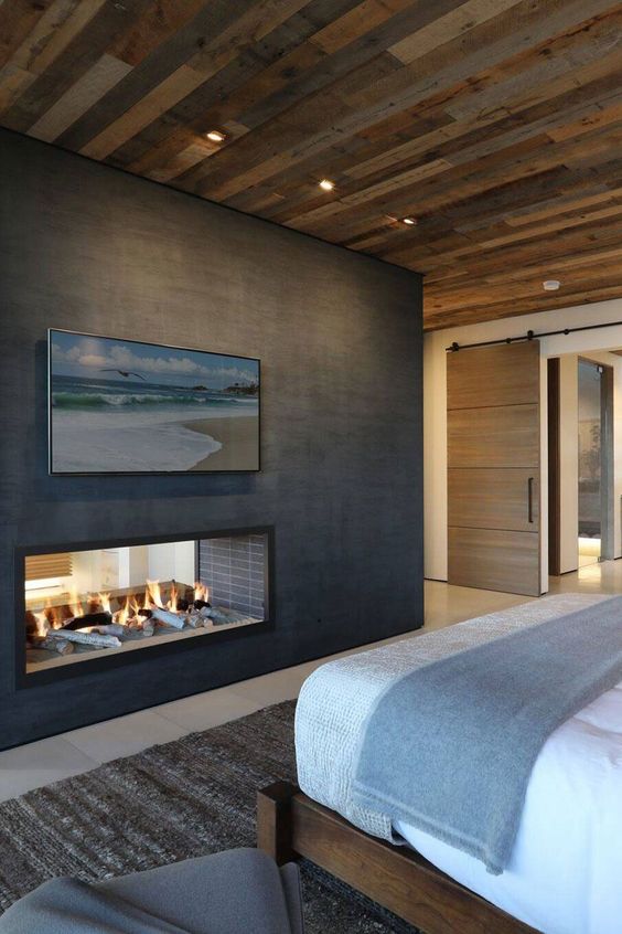 a chalet fireplace witha reclaimed wood ceiling, a bed, a double-sided metal clad fireplace and some artwork
