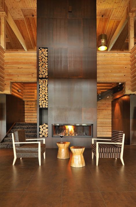 a chalet space with a lage metal clad fireplace with firewood storage, a couple of chairs, side tables and some lights