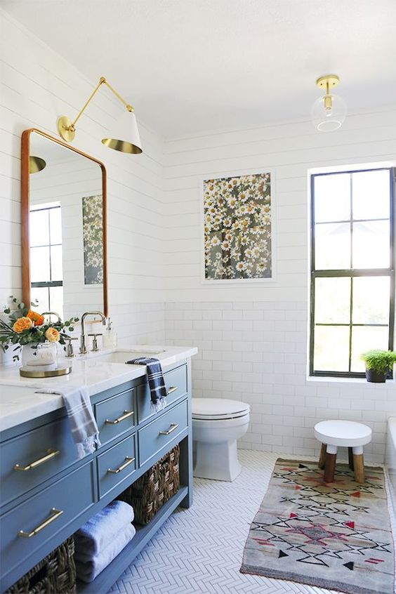 a colorful eclectic bathroom with a blue vanity, a colorful rug and a floral artwork