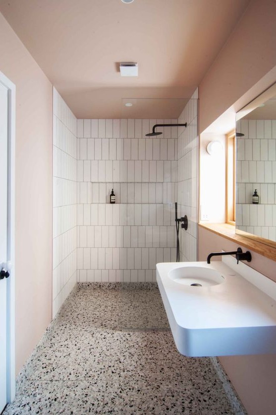 a contemporary bathroom with blush walls and a ceiling, white tiles and appliances and black fixtures