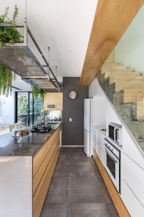 a contemporary white kitchen with sleek built-in storage units in the staircase, a large kitchen island, a metal shelf with greenery